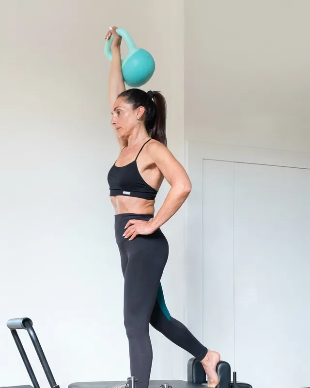 Sabina su un Reformer con un kettlebell sopra la testa